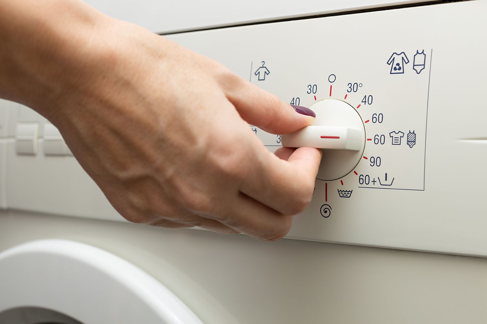 Gros plan d’une main tournant le bouton d’une machine à laver pour sélectionner un cycle de lavage à haute température (60–90°C).