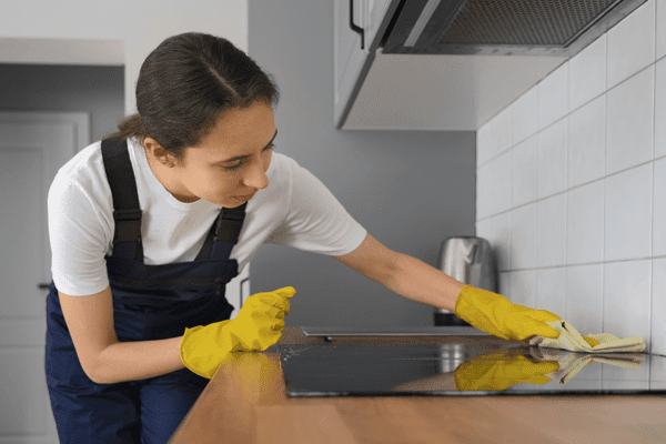 Femme nettoyant soigneusement une surface de cuisine avec des gants pour éviter l’invasion de fourmis.